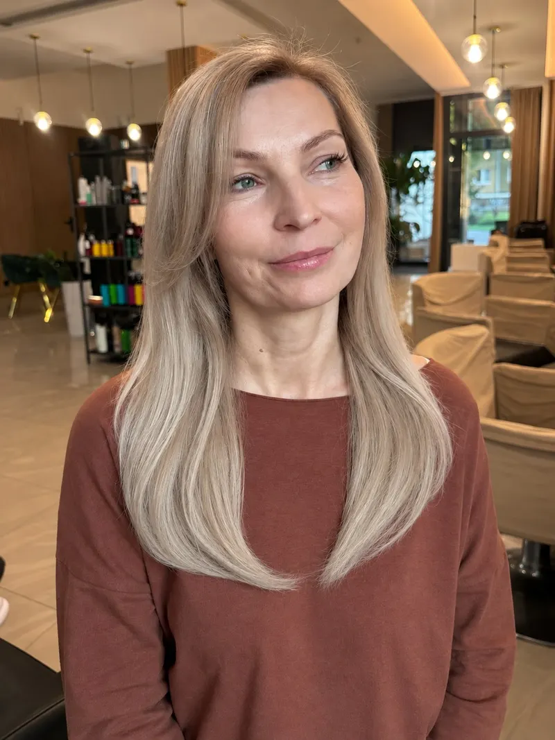Klientka po pięćdziesiątce w długim chłodnobeżowym blondzie z jaśniejszymi pasmami przy twarzy i naturalnie przyciemnioną nasadą